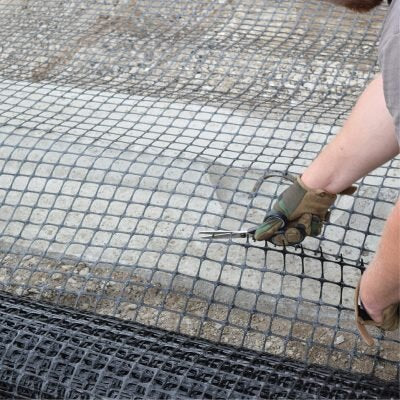 Installer securing black biaxial road base geogrid over compacted gravel base for soil stabilization

