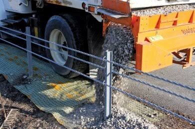 Truck dumping gravel over Biobarrier root barrier fabric installed along a roadway edge
