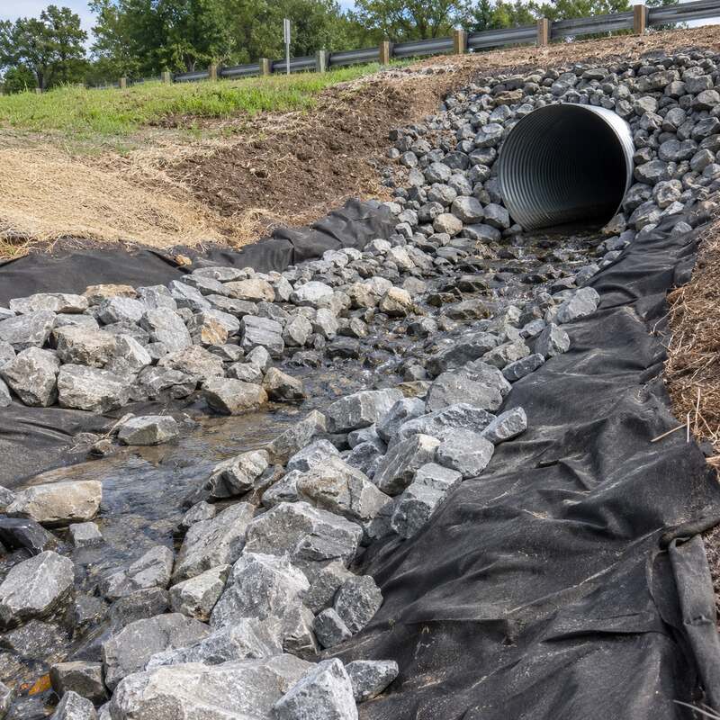Non-woven drainage fabric beneath rip rap stone at a culvert outlet along a roadside ditch
