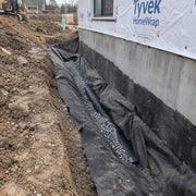 Non-woven drainage fabric wrapping gravel and pipe along a foundation drain trench during new home construction
