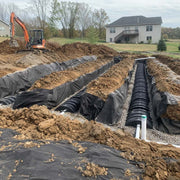 Spunbound drainfield fabric wrapping septic chamber pipe in gravel trenches during installation
