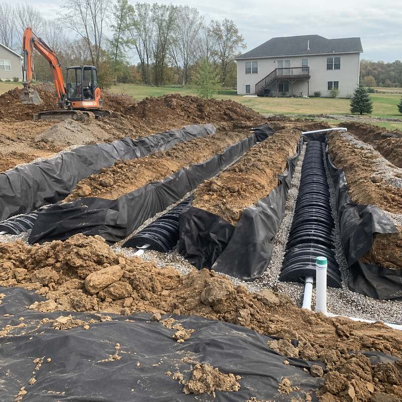 Spunbound drainfield fabric wrapping septic chamber pipe in gravel trenches during installation
