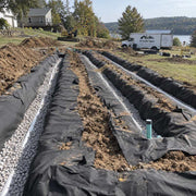 Spunbound drainfield fabric wrapping multiple gravel septic drain field trenches in a large backyard
