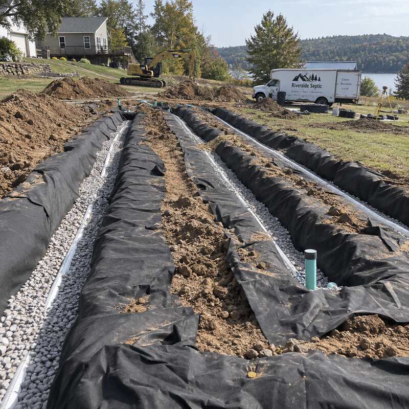 Spunbound drainfield fabric wrapping multiple gravel septic drain field trenches in a large backyard
