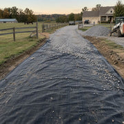 Driveway fabric laid beneath gravel on a horse farm driveway at dusk with horses grazing in the pasture
