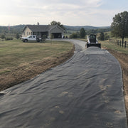 Skid steer spreading crushed gravel over driveway fabric during a rural driveway installation

