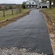 Driveway fabric installed along a long rural driveway with a skid steer and farmhouse in the background
