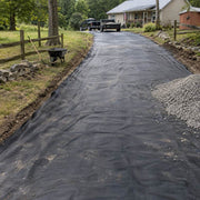 Dump truck delivering gravel onto driveway fabric along a long rural driveway installation
