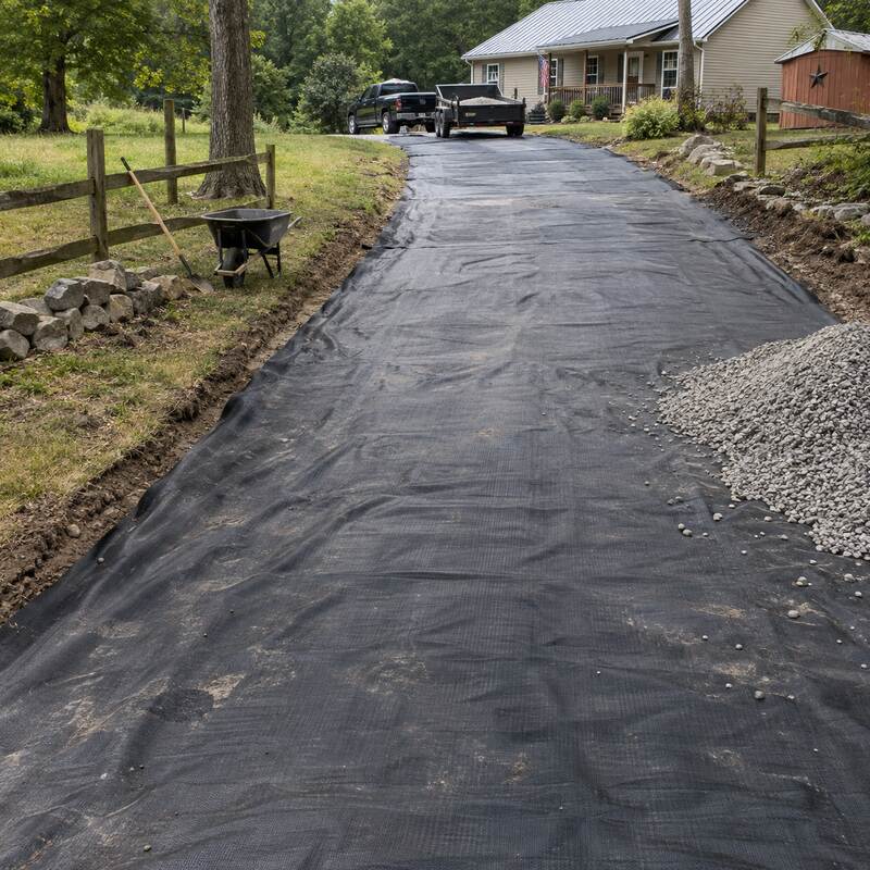 Dump truck delivering gravel onto driveway fabric along a long rural driveway installation
