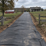 Tractor with a front loader spreading gravel over driveway fabric on a farm driveway installation
