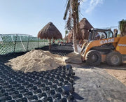 Skid steer filling geocell panels with sand to create a stabilized beach access path near palapas
