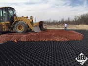 Wheel loader dumping red aggregate onto black geocell panels during a ground stabilization installation
