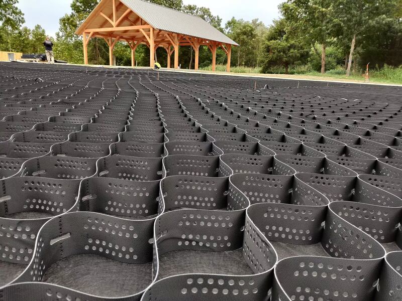 Geocell ground stabilization grid installed over a large gravel parking area near an outdoor pavilion
