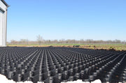 Black HDPE geocell panels installed as parking lot base stabilization outside a metal warehouse building
