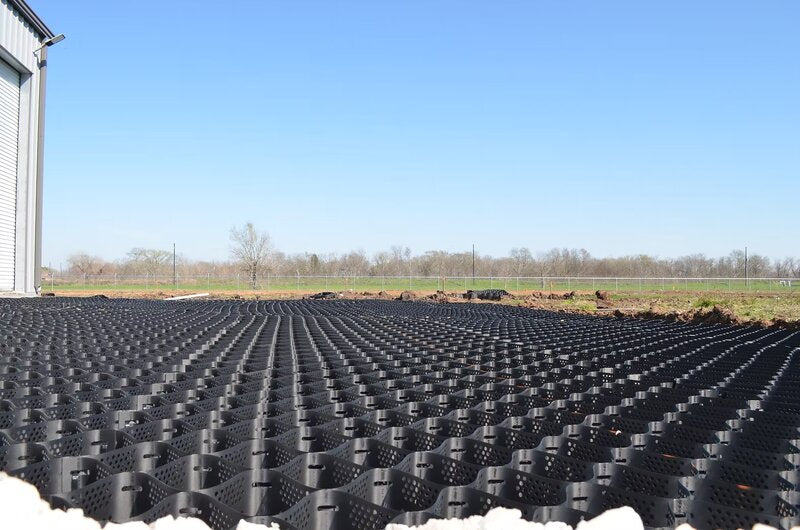 Black HDPE geocell panels installed as parking lot base stabilization outside a metal warehouse building
