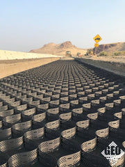 Geocell ground stabilization panels laid across a desert highway construction site with heavy equipment
