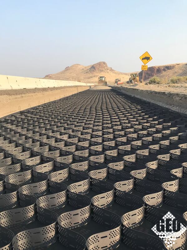 Geocell ground stabilization panels laid across a desert highway construction site with heavy equipment
