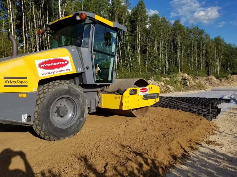 Roller compactor packing sand fill over the edge of a geocell base panel
