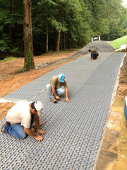 Workers securing gravel paver grid panels along a stone retaining wall edge
