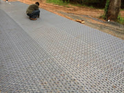 Worker staking down gravel paver grid panels along a long driveway installation
