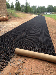 Strip of black gravel paver grid unrolled across a dirt driveway base
