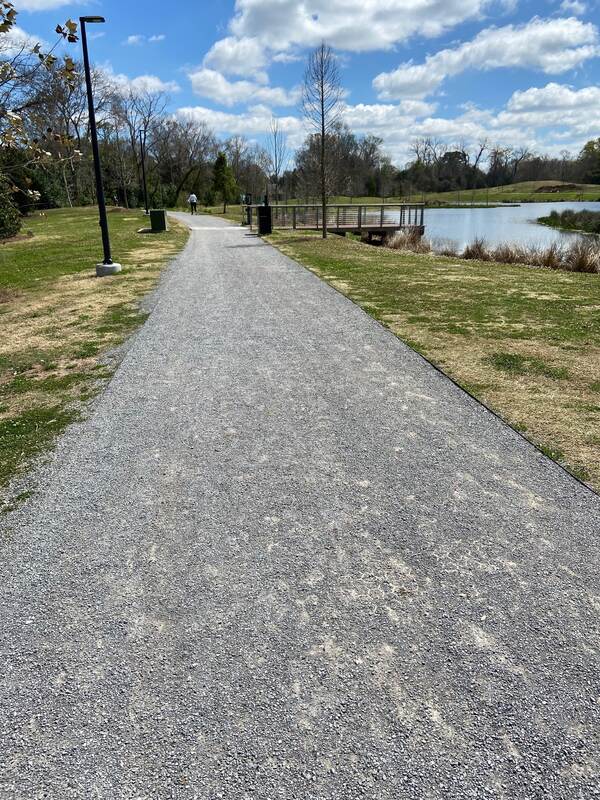 Finished gravel paver walking path through a public park alongside a pond and footbridge
