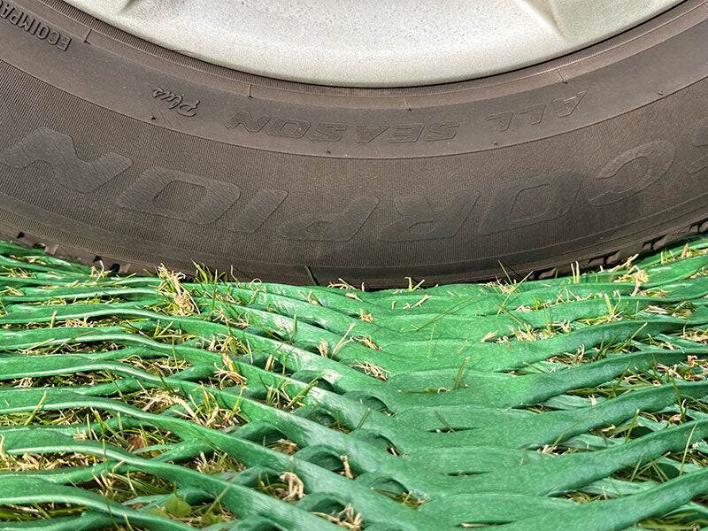 Close-up of a vehicle tire resting on Mudstop grass protection mesh over grass
