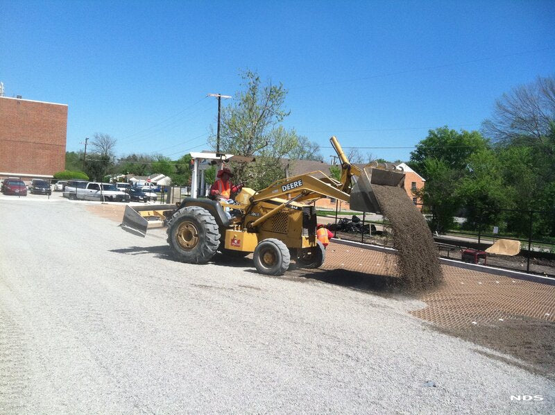 Loader dumping crushed stone onto NDS gravel paver grid panels during installation
