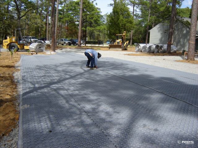 Worker unrolling NDS gravel paver grid over a prepared gravel subgrade during driveway installation
