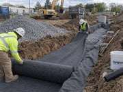 Construction crew installing non-woven fabric in a commercial drainage trench with gravel
