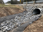 Non-woven fabric lining a roadside drainage ditch with rock leading to a culvert pipe

