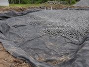 Non-woven fabric lining a large gravel drainage pad with vent pipes at a rural property
