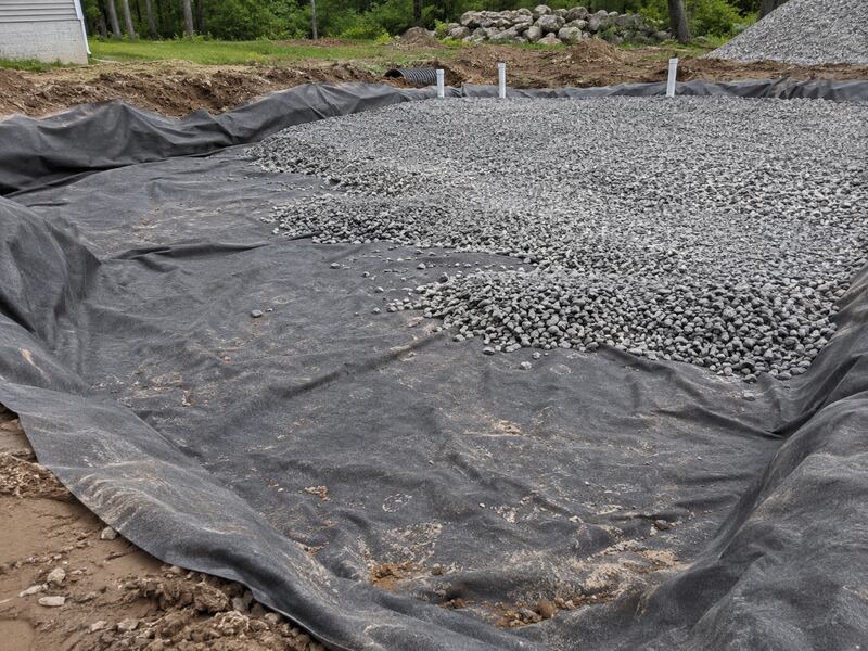 Non-woven fabric lining a large gravel drainage pad with vent pipes at a rural property
