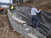Workers wrapping non-woven fabric around drainage gravel behind a block retaining wall
