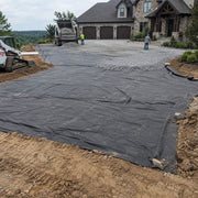 Non-woven geotextile fabric laid beneath gravel during a driveway installation in front of a stone home

