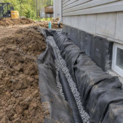 Non-woven geotextile fabric wrapping gravel and drain pipe along a house foundation waterproofing installation
