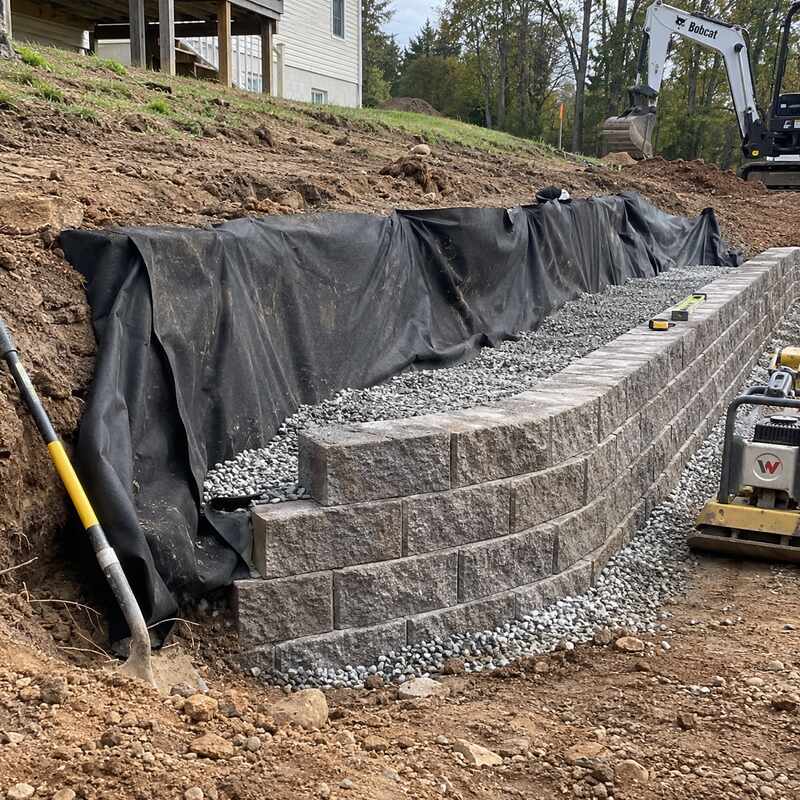 Non-woven geotextile fabric wrapping gravel backfill behind a segmental block retaining wall under construction

