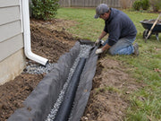 Worker installing non-woven soil filter fabric around a downspout drain trench with gravel
