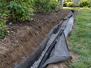 Non-woven soil filter fabric wrapping gravel and drain pipe along a shrub planting bed
