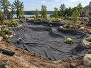 Crew installing pond underlayment fabric in a large pond basin at a lakefront estate
