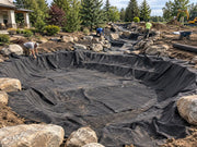 Crew installing pond underlayment fabric along a rock-lined stream and waterfall channel
