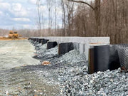 Strata Sleeve-It SD1 drainage sleeves and geogrid mesh installed at the base of a retaining wall under construction
