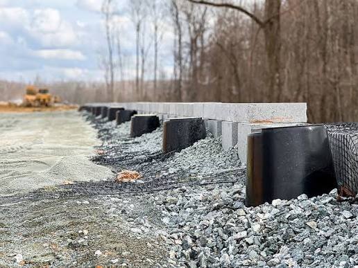 Strata Sleeve-It SD1 drainage sleeves and geogrid mesh installed at the base of a retaining wall under construction
