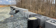 Strata Sleeve-It SD1 drainage sleeves installed behind a segmental retaining wall alongside geogrid reinforcement and gravel backfill
