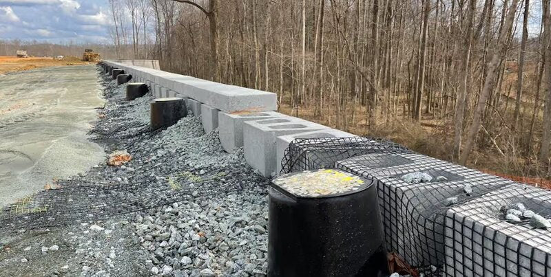 Strata Sleeve-It SD1 drainage sleeves installed behind a segmental retaining wall alongside geogrid reinforcement and gravel backfill
