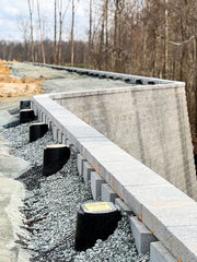 Close-up of Strata Sleeve-It SD1 drainage sleeves set into gravel backfill behind a curved segmental retaining wall

