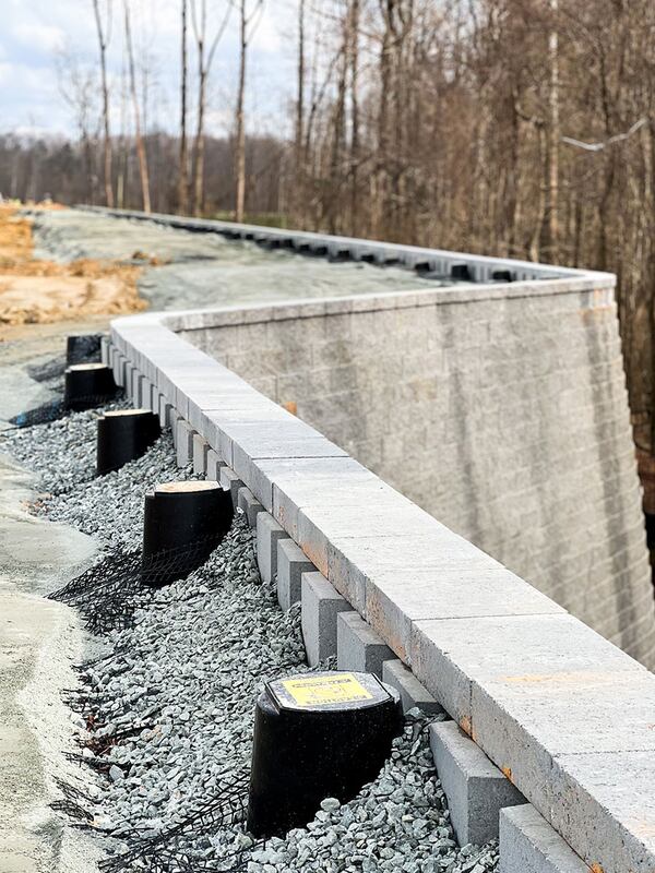 Close-up of Strata Sleeve-It SD1 drainage sleeves set into gravel backfill behind a curved segmental retaining wall

