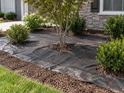 Woven ground cover fabric installed around a tree and shrubs in a house foundation planting bed
