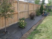 Weed barrier fabric installed along a backyard planting bed beside a wood privacy fence
