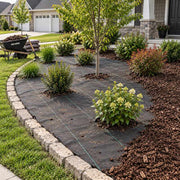 Weed barrier fabric installed in a curved front yard garden bed lined with stone edging and flowering shrubs
